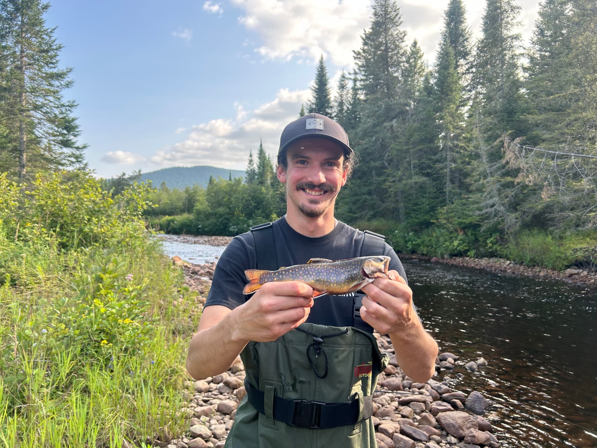 Pêcheur en waders tenant une belle truite mouchetée au bord d'une rivière sauvage du Québec