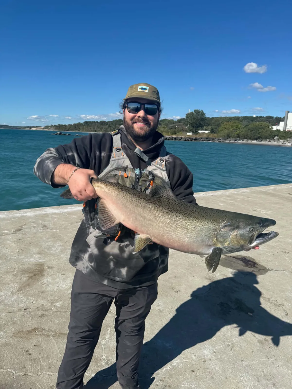 Pêcheur tenant un saumon Chinook argenté sur un quai de béton au bord du lac Ontario, ciel bleu