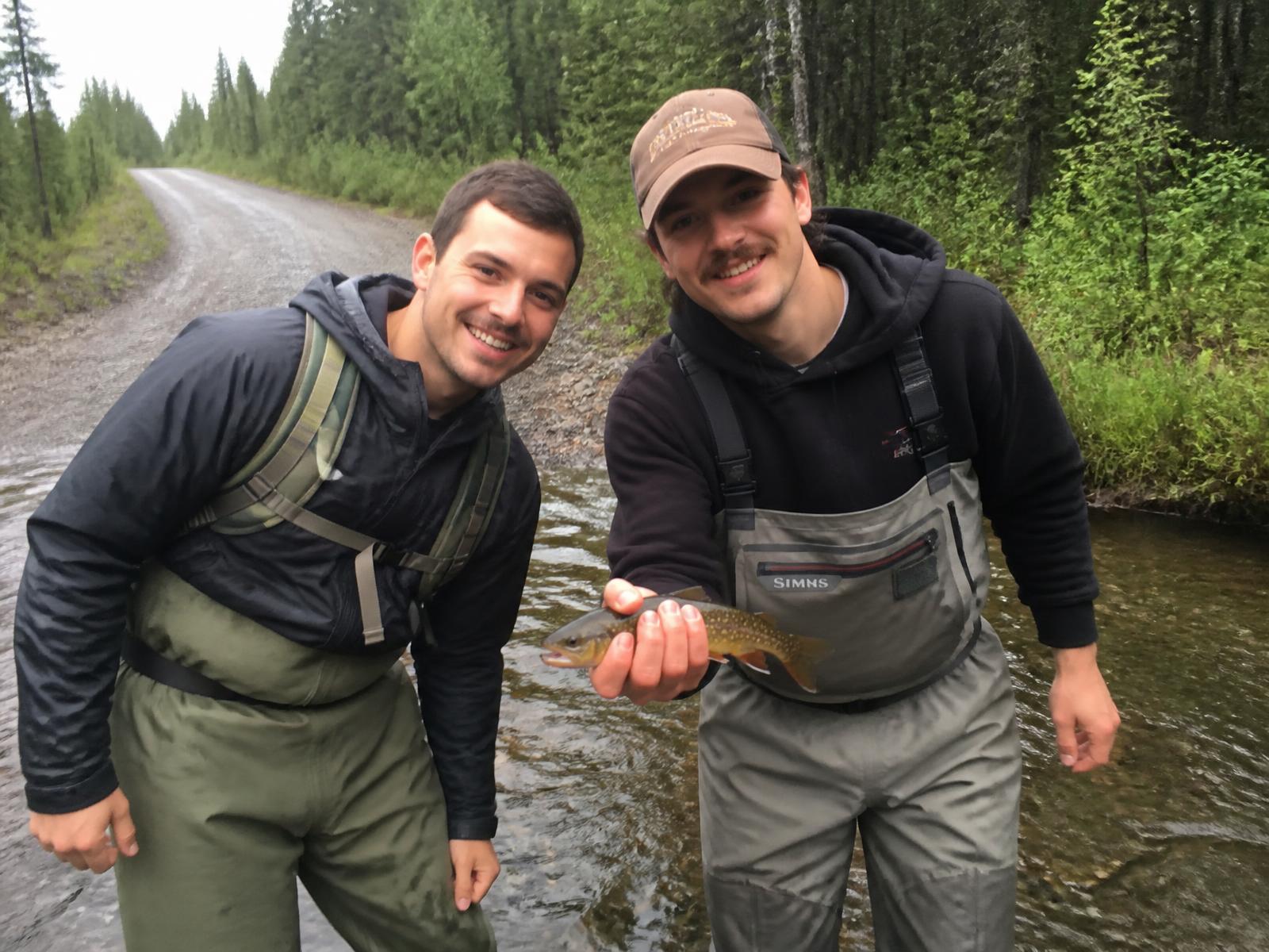 Deux pêcheurs en waders debout dans un ruisseau forestier avec une truite mouchetée dans la main